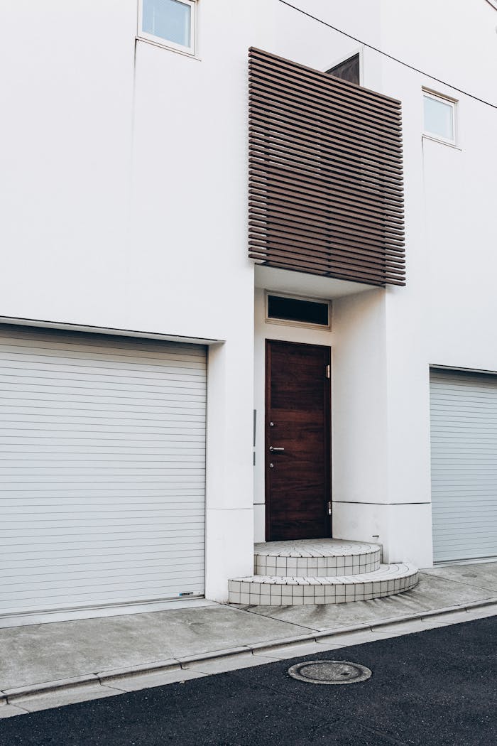 Contemporary white building facade with wooden door and twin garage entrances.